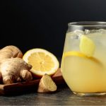 Vaso de jengibre y limón ecológico de Distribuciones Ballester sobre un fondo negro lleno de jengibres y limones.